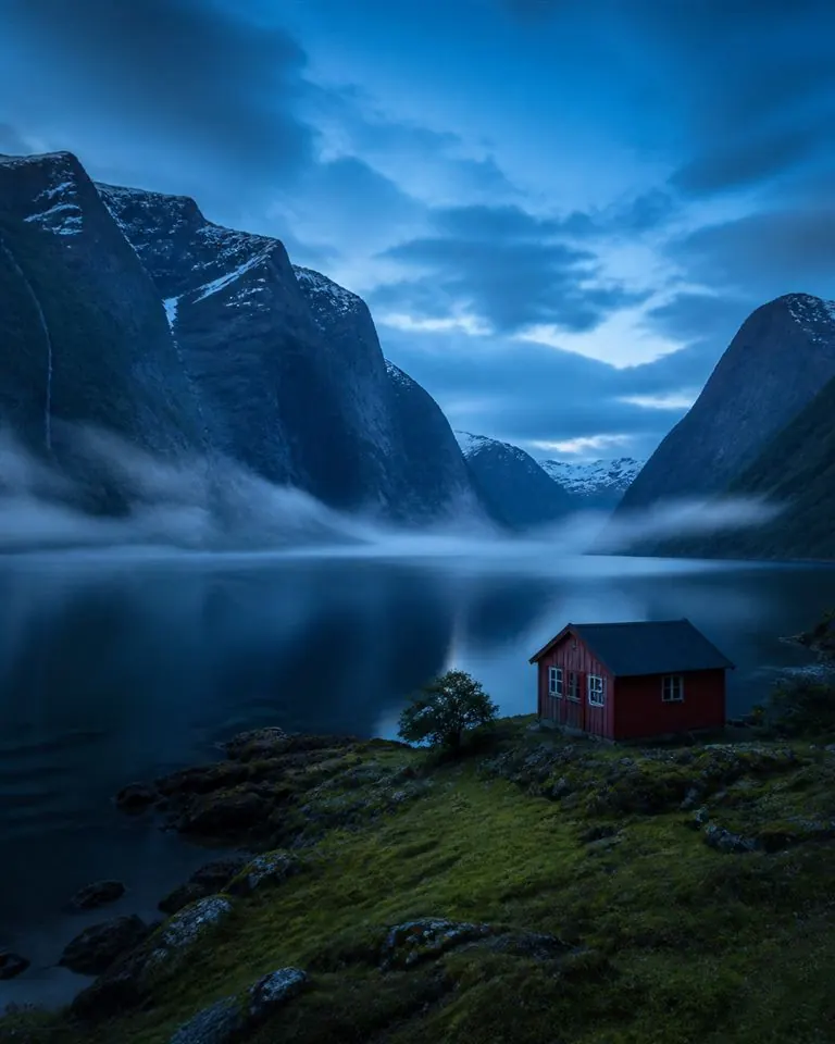 Fjord de Norvège brumeux avec chalet rouge à l’heure bleue