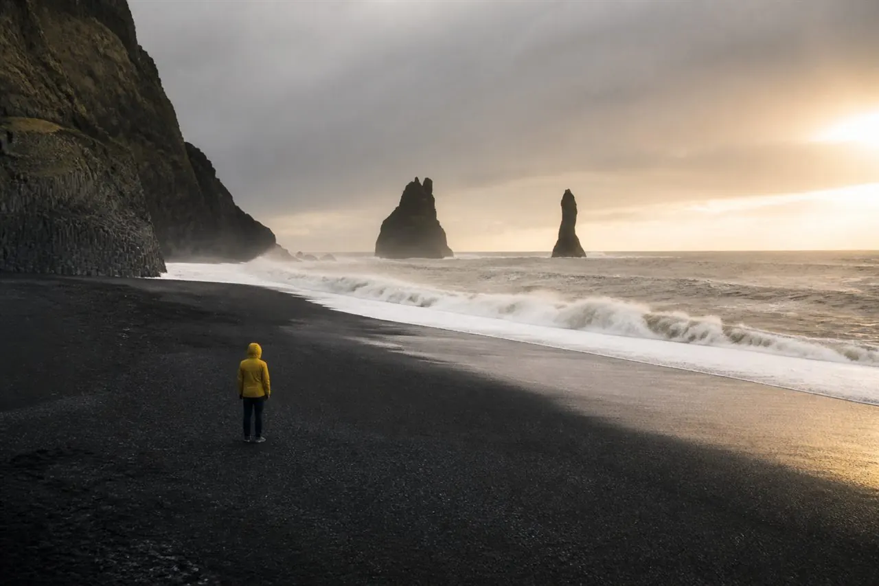 Voyageur sur une plage de sable noir face aux aiguilles rocheuses d’Islande